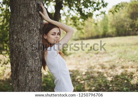 A woman in a t-shirt with raised arms stands near the tree                           