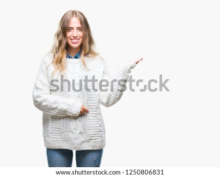 Beautiful young blonde woman wearing winter sweater over isolated background smiling cheerful presenting and pointing with palm of hand looking at the camera.