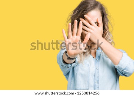 Beautiful young blonde woman over isolated background covering eyes with hands and doing stop gesture with sad and fear expression. Embarrassed and negative concept.