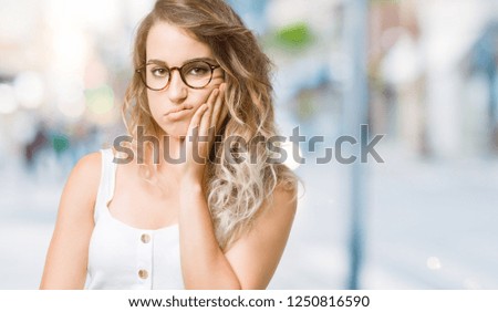Beautiful young blonde woman wearing glasses over isolated background thinking looking tired and bored with depression problems with crossed arms.