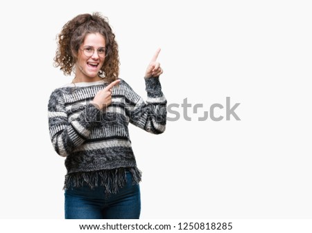 Beautiful brunette curly hair young girl wearing glasses over isolated background smiling and looking at the camera pointing with two hands and fingers to the side.