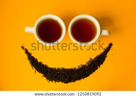 Two cups and a smile of dry tea leaves on a yellow background. December 15th International Tea Day was founded to draw attention to the problems of selling tea, the conditions of tea production worker Royalty-Free Stock Photo #1250819092