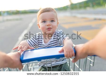 Beautiful and adorable baby in shopping cart. Father and son in shopping. Baby boy sitting in the shopping trolley outside. Family, childhood, fatherhood and people concept