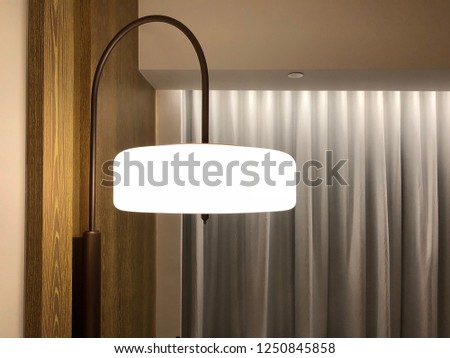 diffuse fabric shade of wall lamp surface mounted onto the wooden backdrop wall in front of the beige curtain in the hotel room