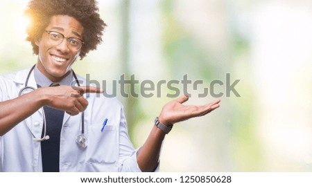Afro american doctor man over isolated background amazed and smiling to the camera while presenting with hand and pointing with finger.