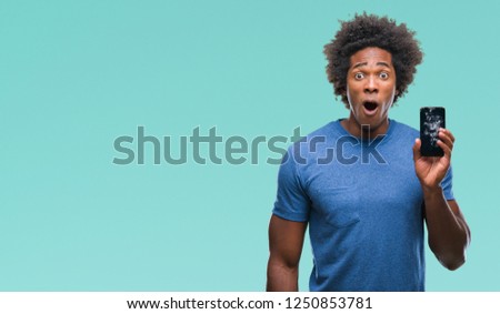 Afro american man holding broken smartphone over isolated background scared in shock with a surprise face, afraid and excited with fear expression