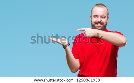 Young caucasian hipster man wearing red shirt over isolated background amazed and smiling to the camera while presenting with hand and pointing with finger.