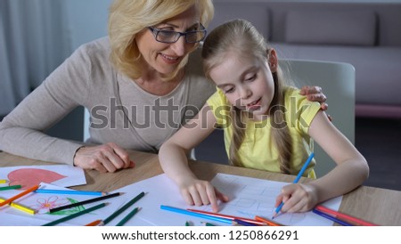 Grandmother hugging granddaughter, cute girl painting house with colored pencil