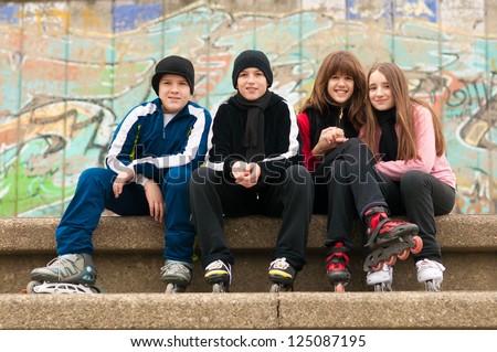 Group of happy teenagers sitting on the street in roller skates on cloudy autumn day.