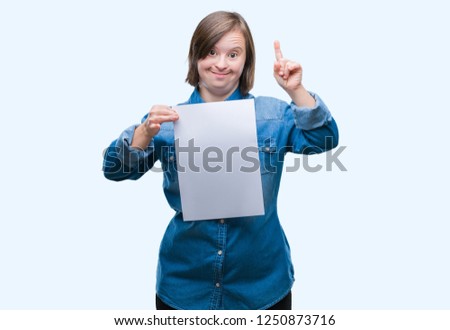 Young adult woman with down syndrome holding blank paper sheet over isolated background surprised with an idea or question pointing finger with happy face, number one