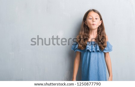 Young hispanic kid over grunge grey wall making fish face with lips, crazy and comical gesture. Funny expression.