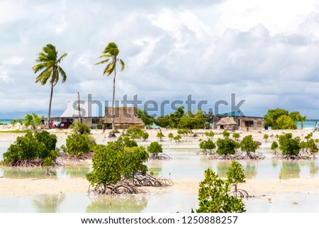 Village on South Tarawa atoll, Kiribati, Gilbert islands, Micronesia, Oceania. Thatched roof houses. Rural life on a sandy beach of remote paradise atoll island under palms and with mangroves around.  Royalty-Free Stock Photo #1250888257