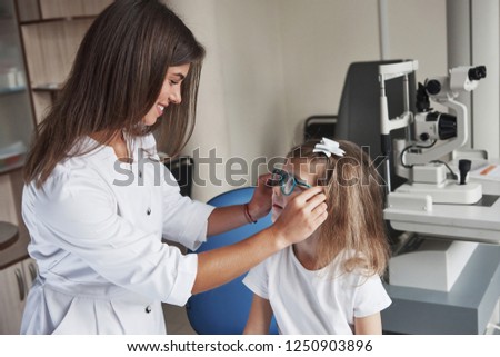 Looking at each other. Little girl tries new blue glasses in ophthalmologic office with female doctor.