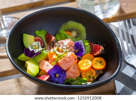 Exotic ceviche of salmon served with fresh avocado, cumquat, kiwi fruit, figs decorated with pansy flowers