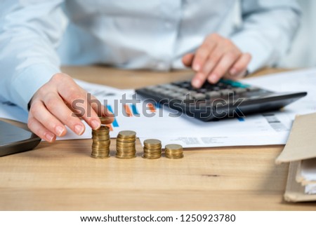 Close up cropped investor or sale manager lady in her formal wear shirt she put money in pile sit behind table in bright loft interior workstation count tax on invoice focus on hand with coins Royalty-Free Stock Photo #1250923780