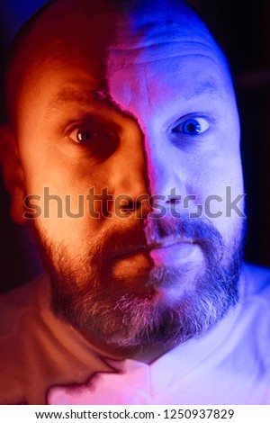 the pensive, surprised and mysterious face of a man, illuminated by red and blue light..