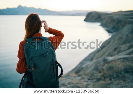 A woman with a backpack on the background of the rocky mountains and the sea                     