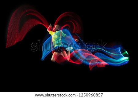 The one caucasian young teenager girl playing badminton at studio. The female teen player on black background in motion with flashes of  neon light