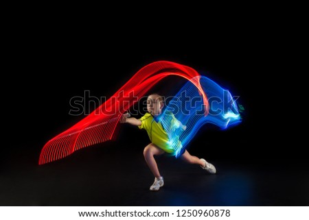 The one caucasian young teenager girl playing badminton at studio. The female teen player on black background in motion with flashes of light