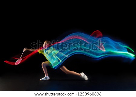 The one caucasian young teenager girl playing badminton at studio. The female teen player on black background in motion with flashes of light