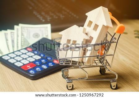 Wooden houses in a supermarket trolley, money and a calculator. Real Estate Market Analytics. Real estate concept. Sale and purchase of property. Rent apartment. Realtor Services. Selective focus
