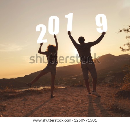 Silhouette of a couple in love standing near a seaside cliff, holding numbers 2019 and looking at a beautiful sunset at Valtos beach in Parga, Greece