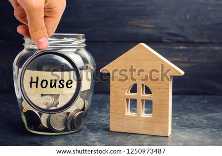 A glass jar with coins and a wooden house and the inscription "House". The accumulation of money to buy a house. Rent an apartments. Purchase a home. Rental housing. Saving money