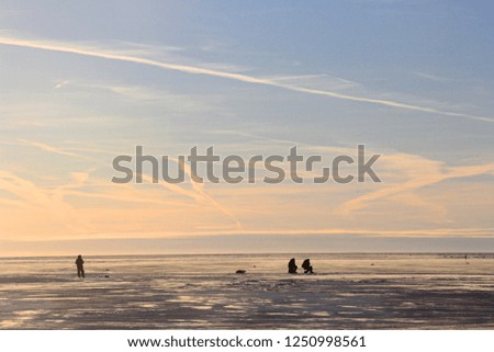  ice fishing angler silhouettes on ice and beautiful yellow sunset with lines from airplane in Pärnu bay, Baltic sea, Pärnu County, Estonia