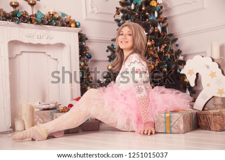 gentle woman in pink xmas sweater and tutu children's skirt enjoys near a girl's Christmas tree and a white fireplace alone in the cute room