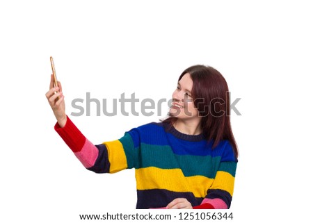 Happy young woman taking a selfie using her mobile phone isolated over white background. Girl wearing colorful sweater having fun.