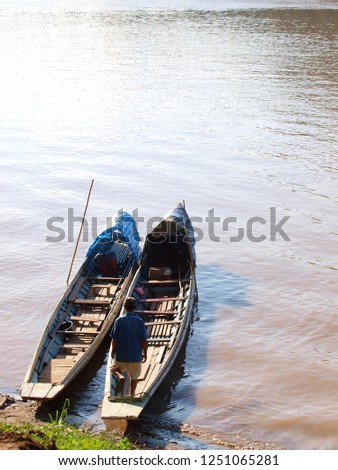 an unidentified person standing on peaceful natural colour wooden boats closeup crop view on brown water river bank under warm summer sunlight for unseen natural adventure vacation tour advertisement