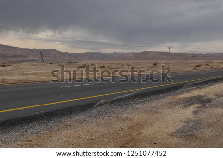 Deserted road between the mountains without people or cars on a wintery day. The picture was taken on a road trip in Israel. a few desert plants and electric poles are in sight