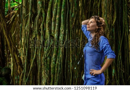 portrait of nice young woman is taking picture in the jungle with lians. The girl stands by the tree beside her. The loneliness of a girl who is alone in the jungle