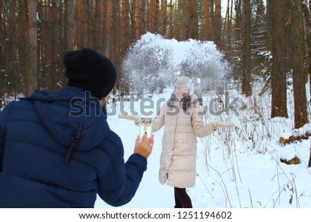 A young girl throws snow in the air and a man shoots it on a smartphone. Background. Landscape.