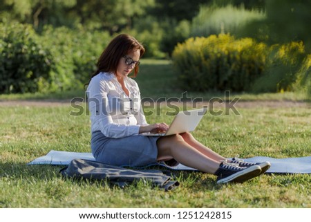 Beautiful big girl lying on the green grass in park with her laptop and working. Student girl looking at the computer screen.