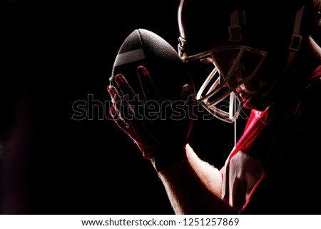 Side view of American football player standing with rugby helmet and ball