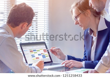 Team planning a meeting with calendar on computer, search time slot between events, tasks, and appointments, busy business people using time management tool to organize work, colleagues in office