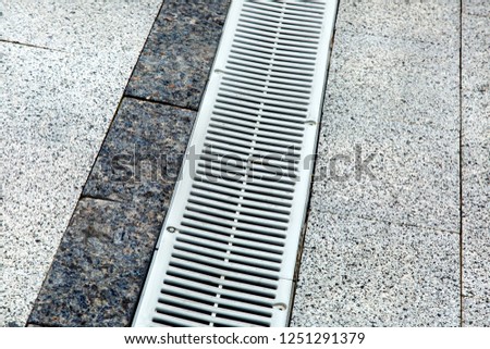 metal gutter on a pedestrian sidewalk grey tiles close-up.