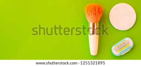Brush for applying blush and cotton sponge discs with removable razor cartridge on an oblong green background with space for text. Creative idea for beauty products and make-up. Flat lay.