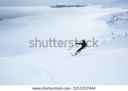 A woman is skiing on the slope. Powder day in ukrainian Carpathian mountains. Mountain range over the clouds.