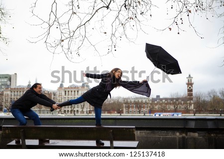 Picture of a couple in a windy day holding an umbrella.