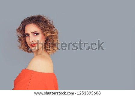Envious beauty. Jealous woman looking back to the side disgusted frowning pretty woman with curly hair in red dress isolated on light grey gray background wall. Negative human emotion face expression