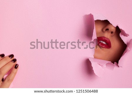 View of bright lips through hole in pink paper background. Make up artist, beauty concept. Ready to new year party. Cosmetics sale. Beauty salon advertising banner with copy space.