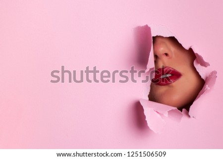 View of bright lips through hole in pink paper background. Make up artist, beauty concept. Ready to new year party. Cosmetics sale. Beauty salon advertising banner with copy space.
