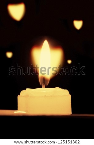 White candles, on a black background, flashing a heart-shaped dreamy glow.