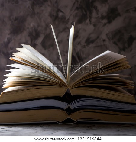 A stack of open books with flipped pages on a gray background. Learning reading and self-development concept