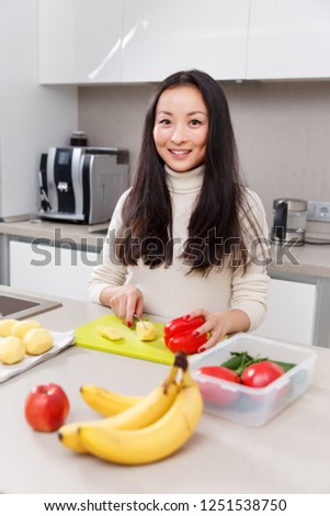 Photo of young brunette cutting potatoes at table with vegetables and fruits