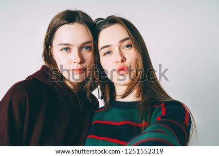 Two sisters twins beautiful girls in casual taking selfie on frontal camera of smartphone on grey background isolated