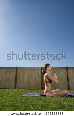 Side view of a woman doing yoga in yard with blue sky