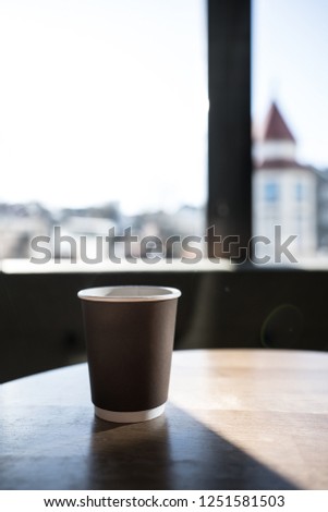 Isolated coffee in paper cup setting on wood teak table in cafe with natural light through the window/ Morning time /space for advertising / standalone cup /close up object with background /